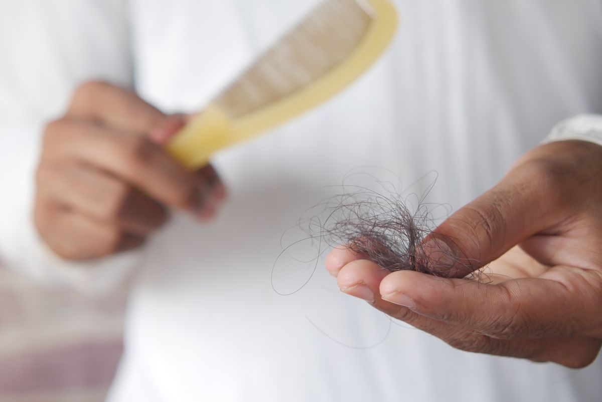 Close-up of hair strands in a hand next to a comb, showing hair loss